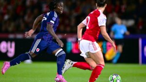 Tabitha Chawinga in all dark blue kit and pink boots is pictured mid-stride running with a football which has a star motif on it during a match between Lyon and Arsenal in the Uefa Women's Champions League. Chawinga has her head up and is looking at an opponent who is seen from behind in red and white kit coming to challenge her