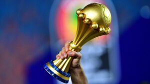 A hand holds up the gold Africa Cup of Nations trophy against a blurred background